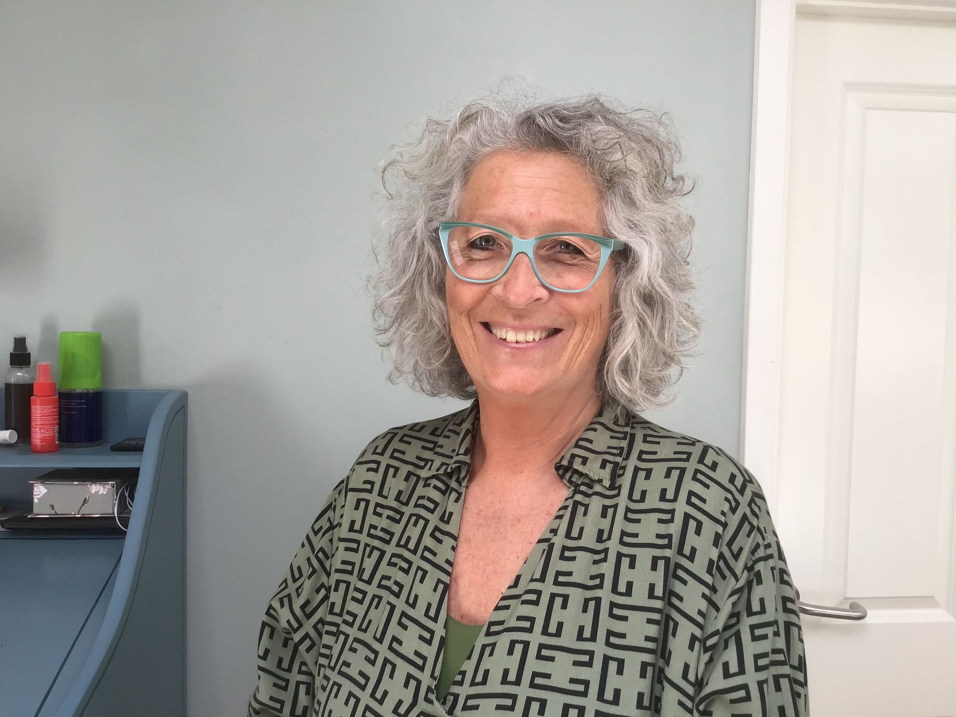 En kvinde med krøllet hår og briller smiler til kameraet.