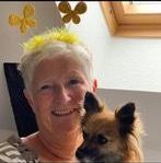 En kvinde holder en lille hund i sine arme og smiler.