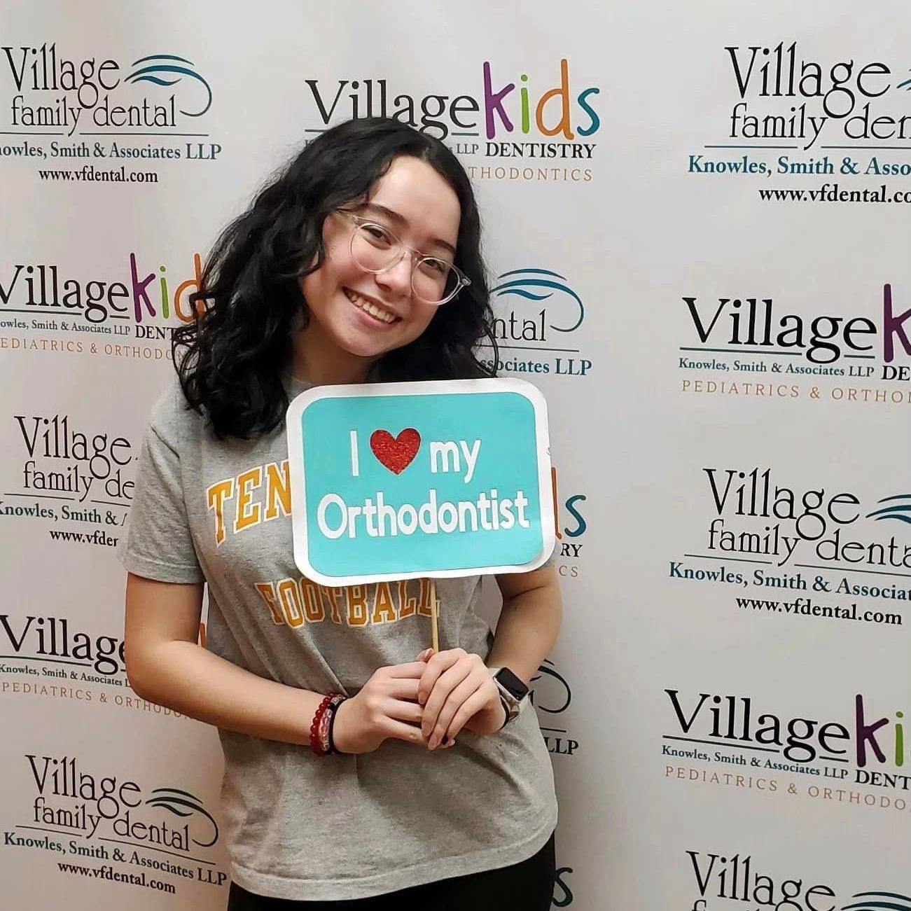 A woman is holding a sign that says `` i love my orthodontist ''.