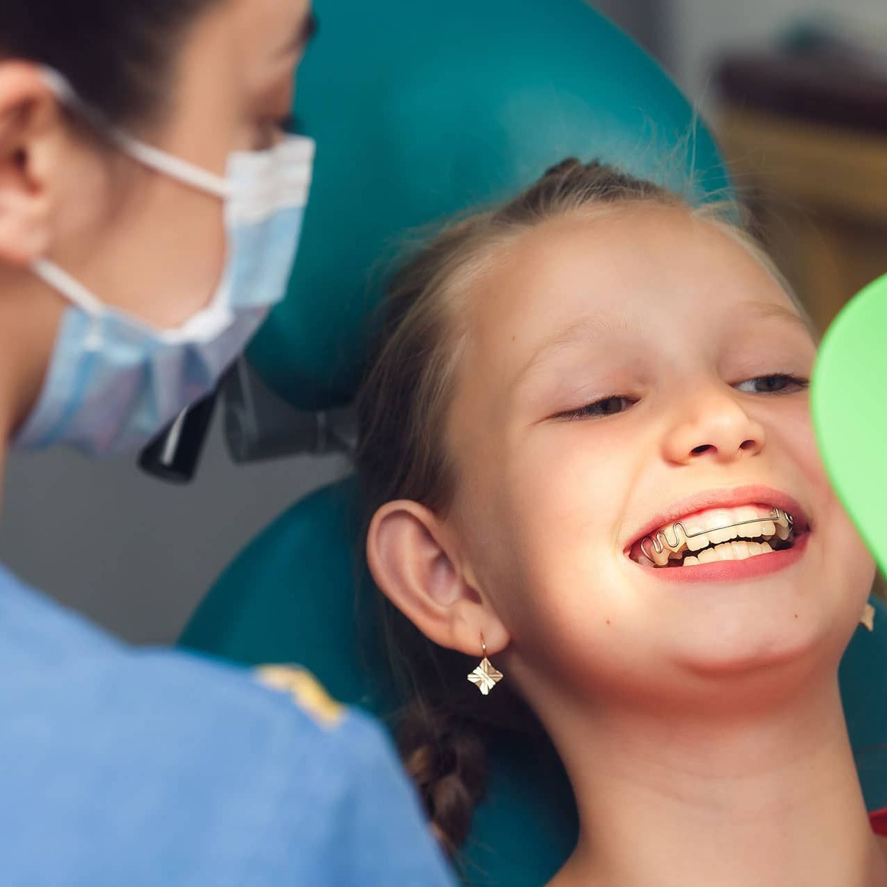 A little girl with braces on her teeth is smiling at the dentist