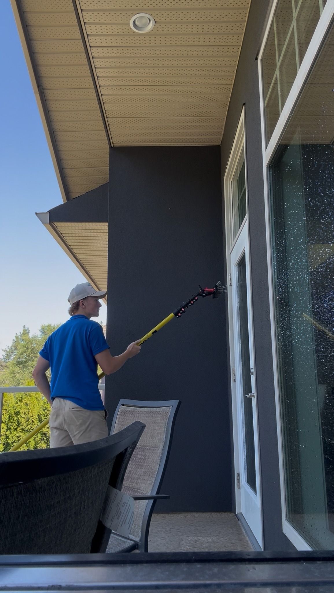Man cleaning window with a long-handled brush on a sunny day.