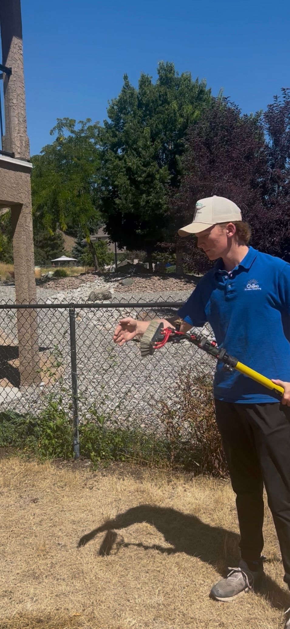 Man spraying a chain-link fence with water on a sunny day.