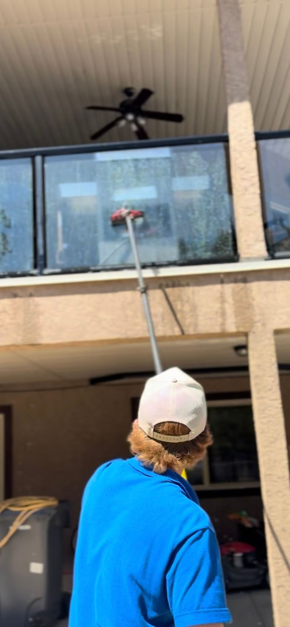 Person in blue shirt washing a window with a long brush.