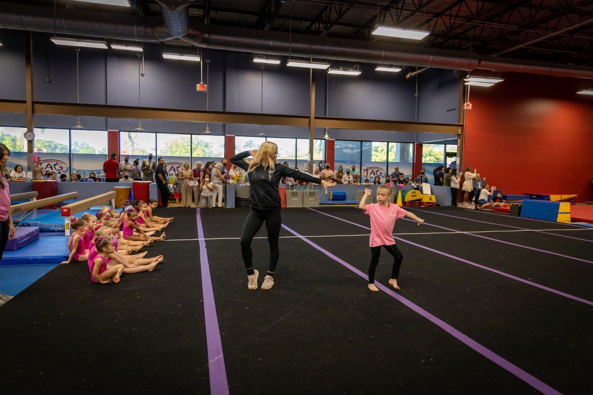 A woman is teaching a group of young girls how to do gymnastics in a gym.