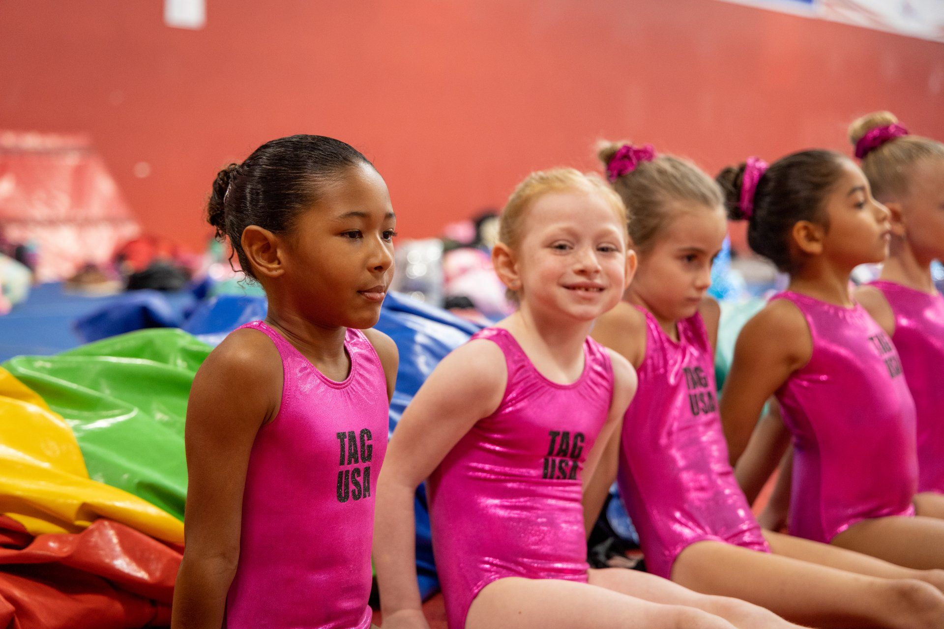 A group of young girls in pink leotards are sitting on the floor.