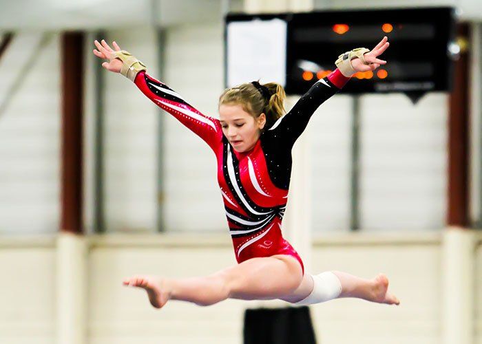 A girl in a red and black leotard is jumping in the air