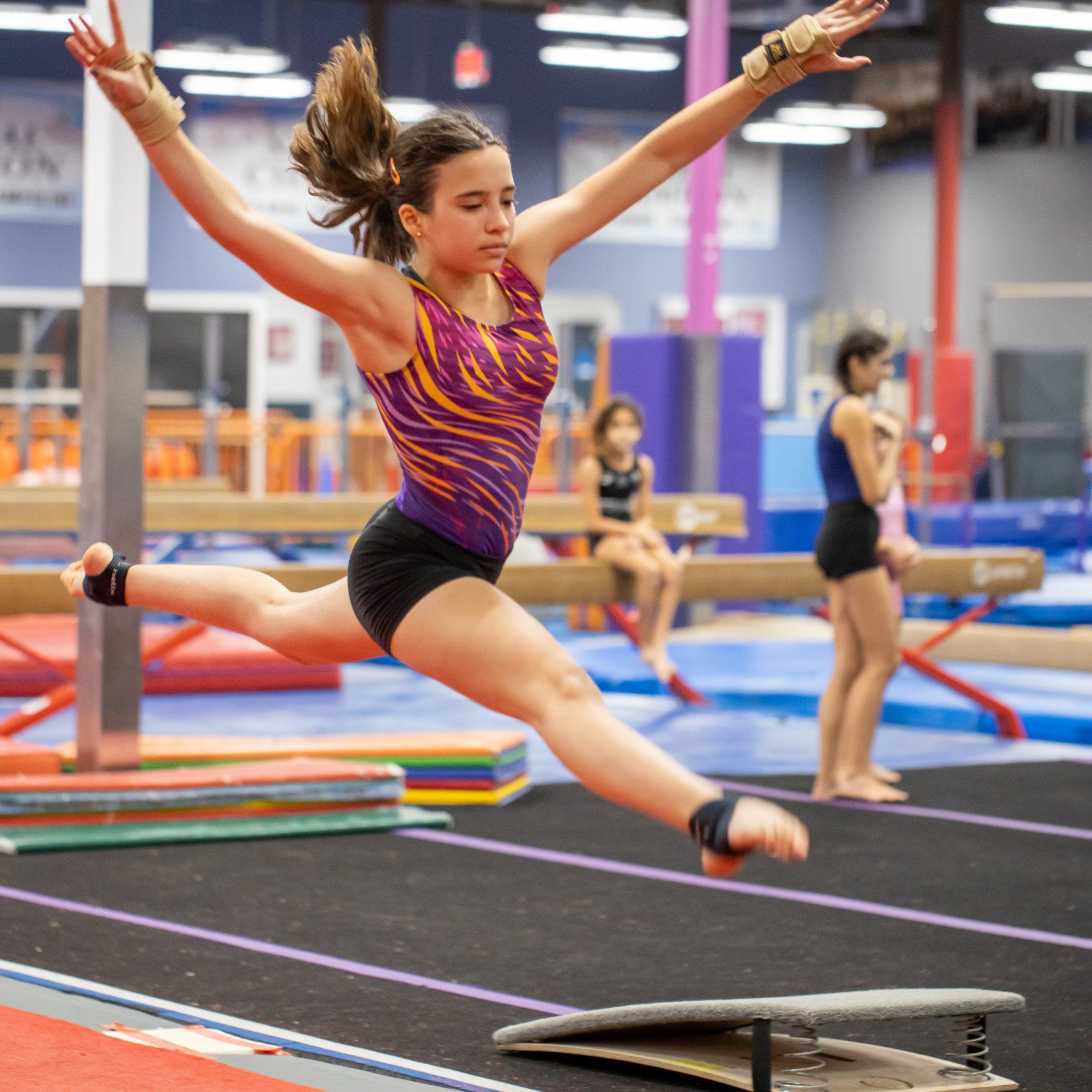 A female gymnast is jumping over a balance beam