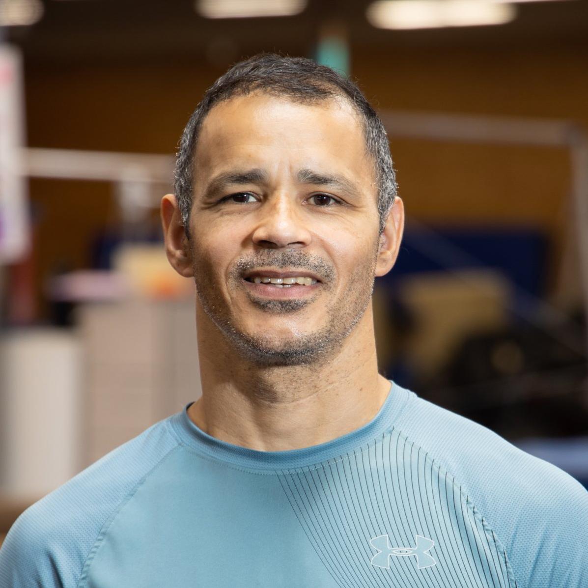 A man wearing a blue under armour shirt is smiling for the camera.