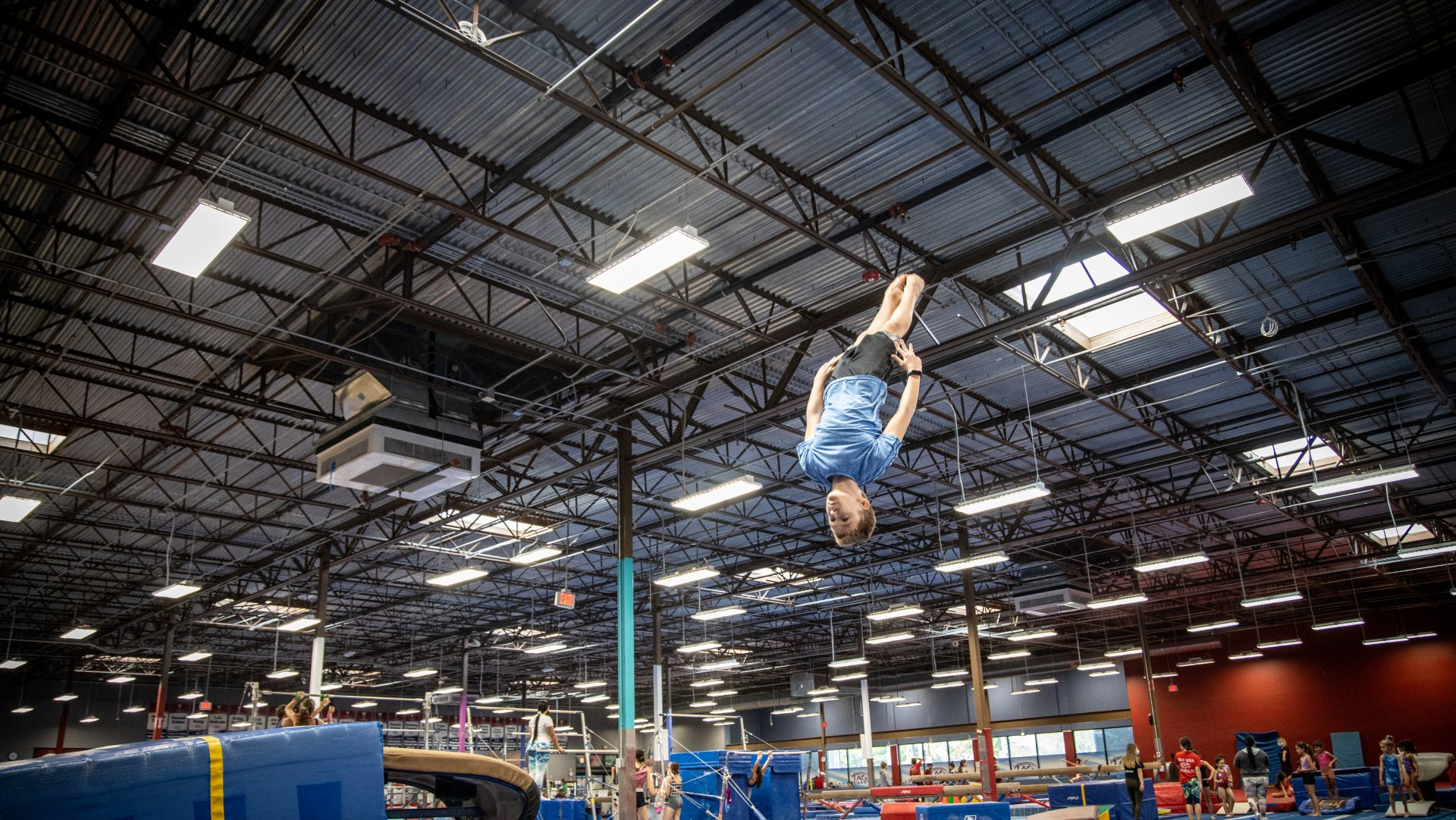 A girl in a blue leotard is standing on a balance beam