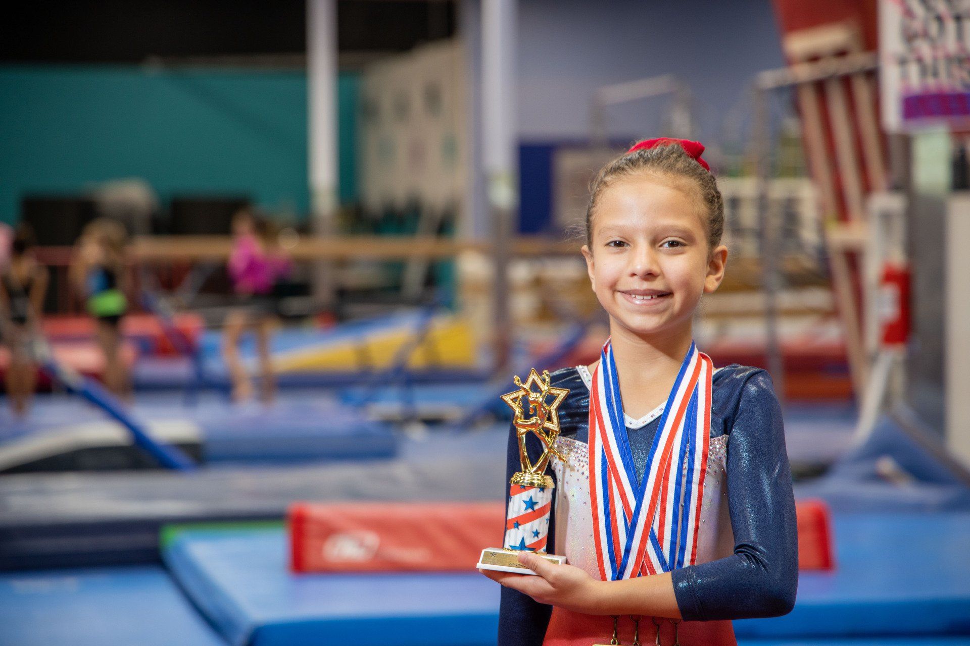 A young girl is holding a trophy and medal in a gym.