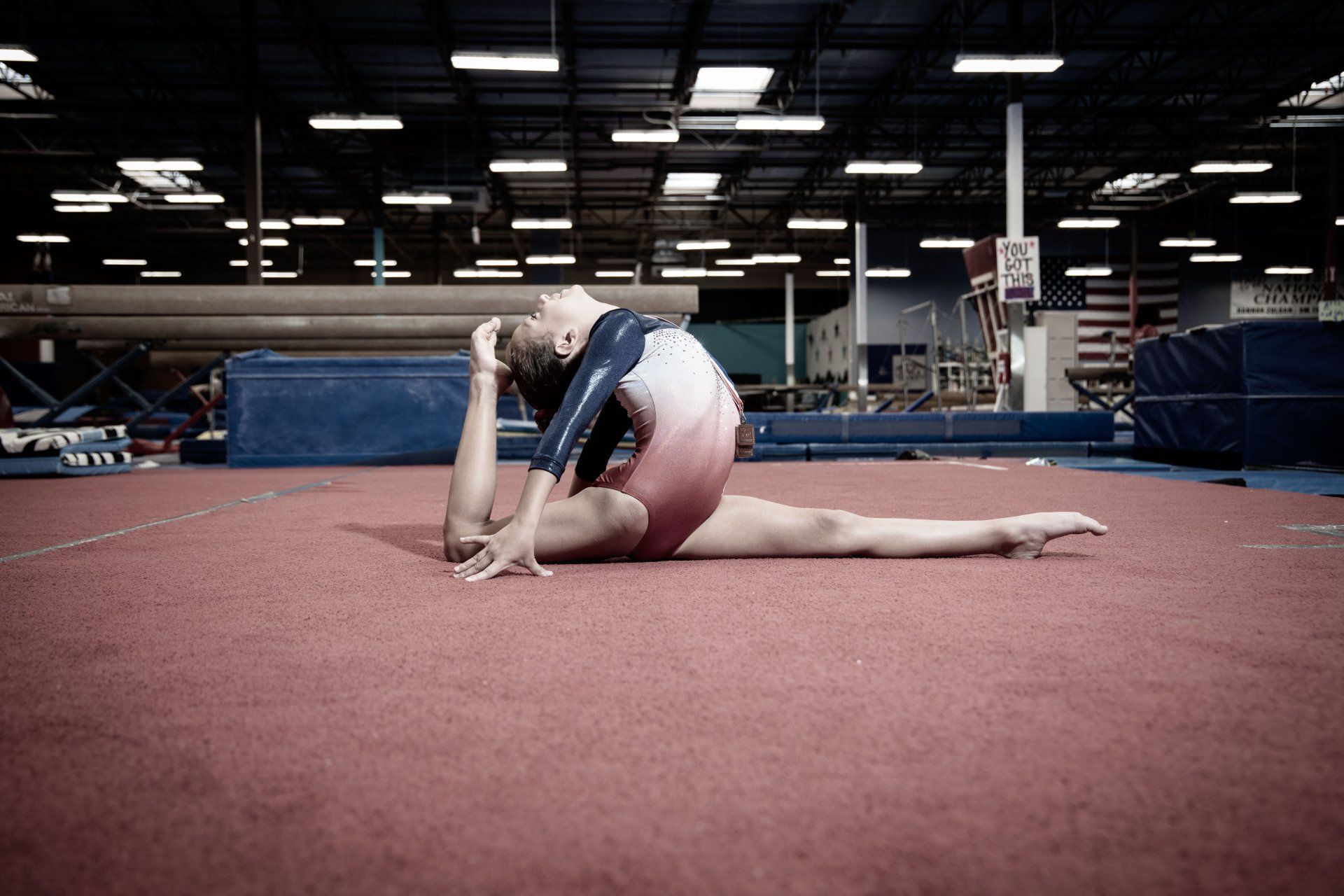 A female gymnast is doing a split on the floor in a gym.