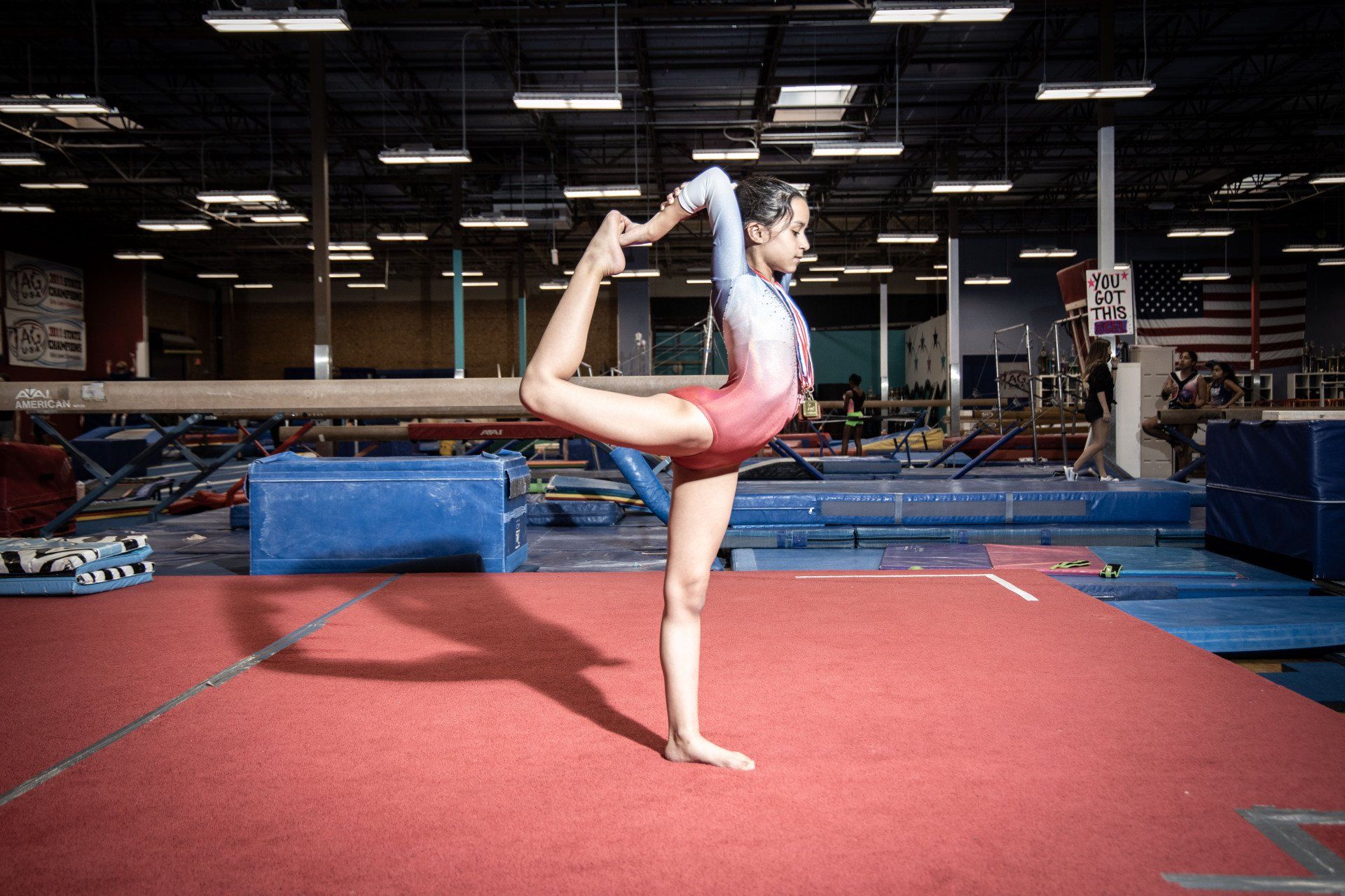 A female gymnast is doing a yoga pose on a balance beam in a gym.