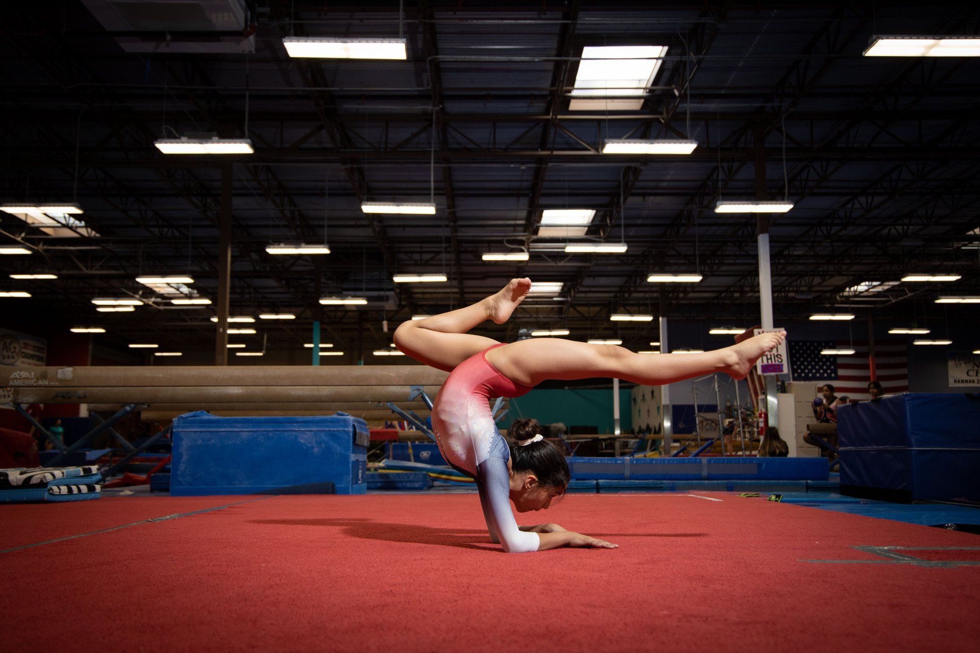 A young girl is doing a handstand on a balance beam in a gym.