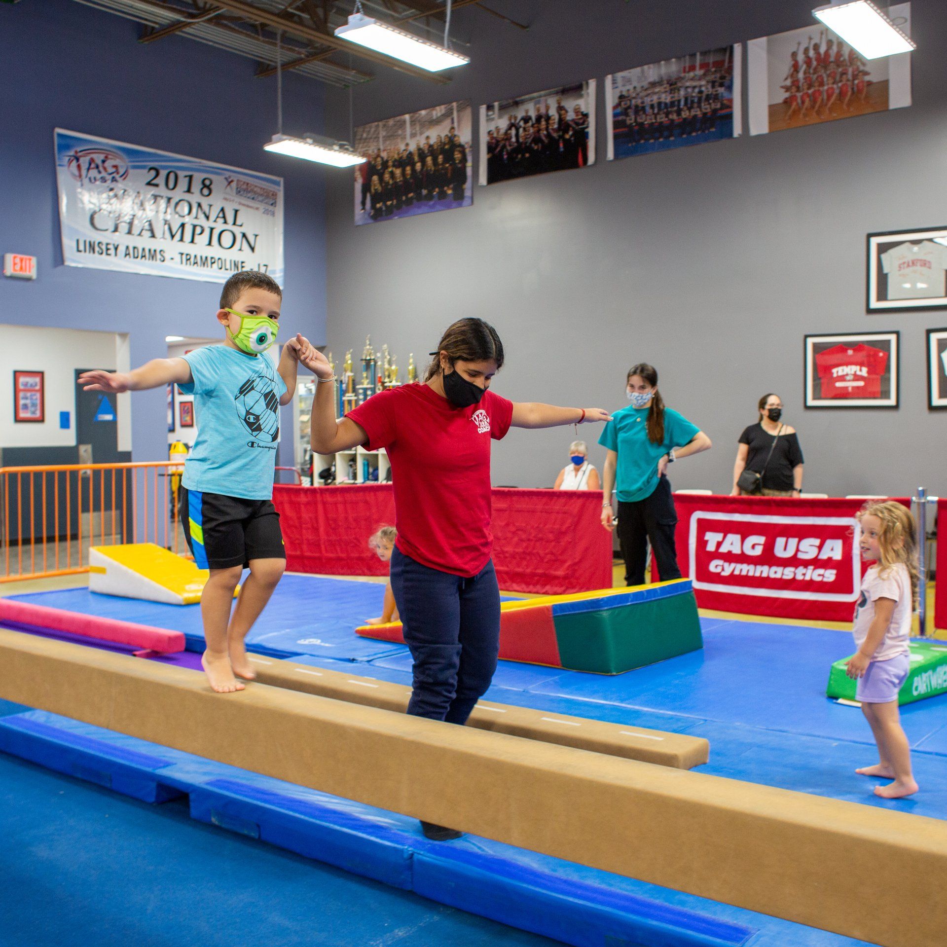 A group of people are standing on a balance beam in a gym.