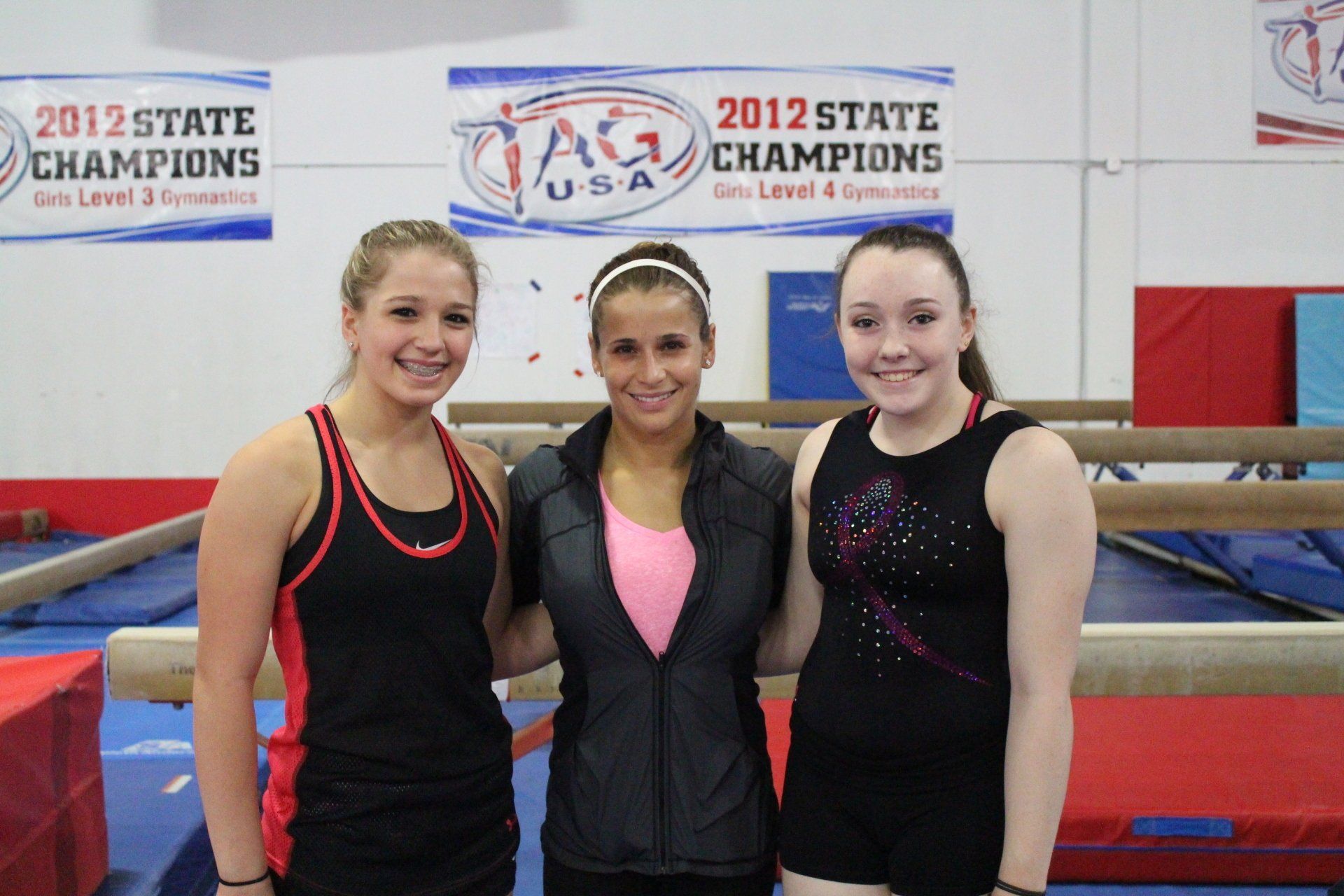 Three girls are posing for a picture in front of a sign that says 2012 state champions