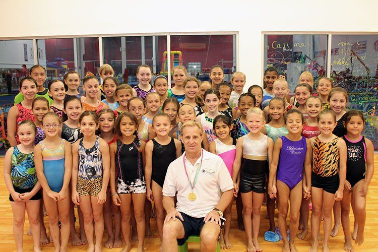 A man is sitting in front of a group of young girls in a gym.