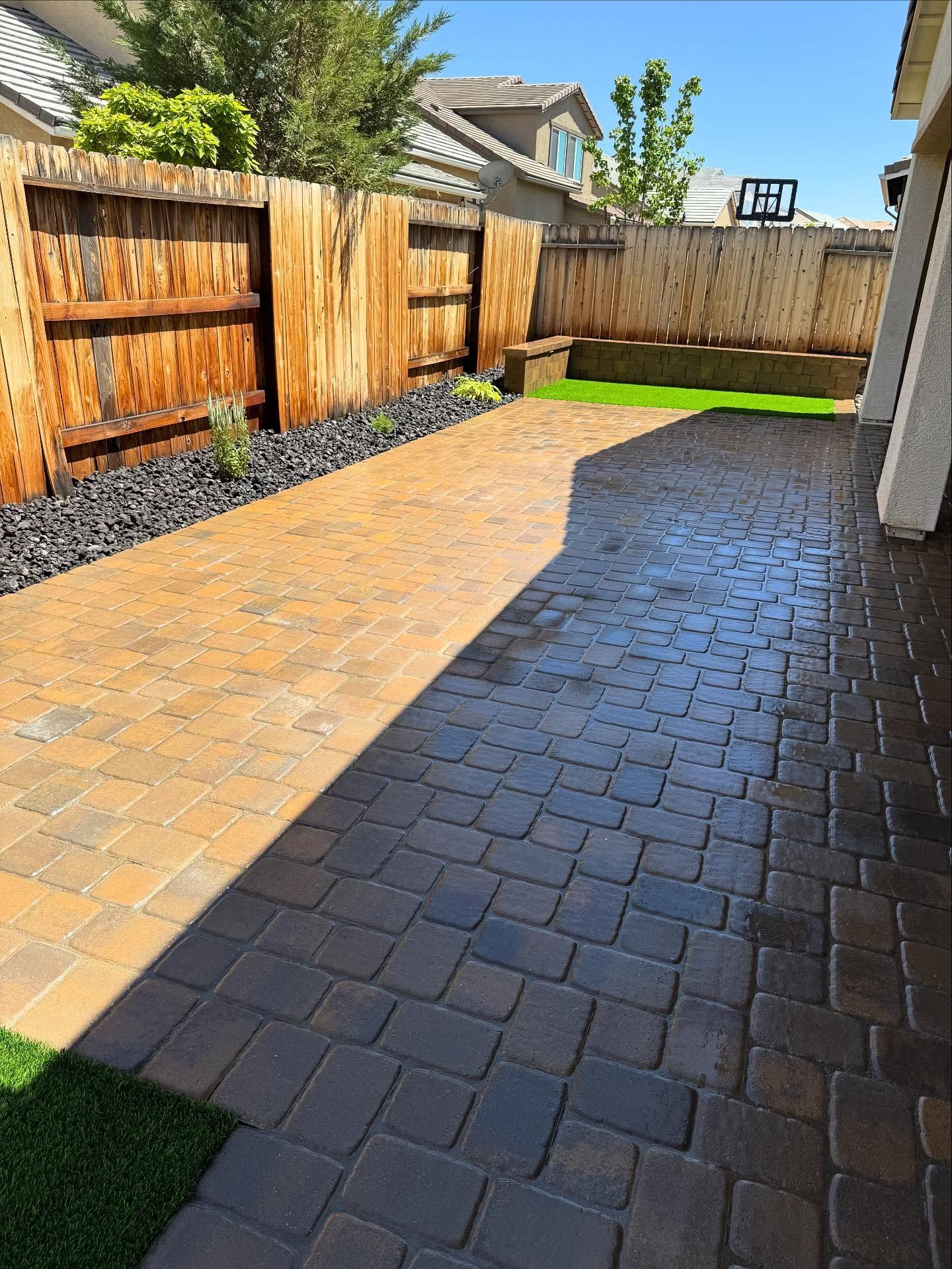 Backyard with brick patio, black rock border, wooden fence, and artificial turf.