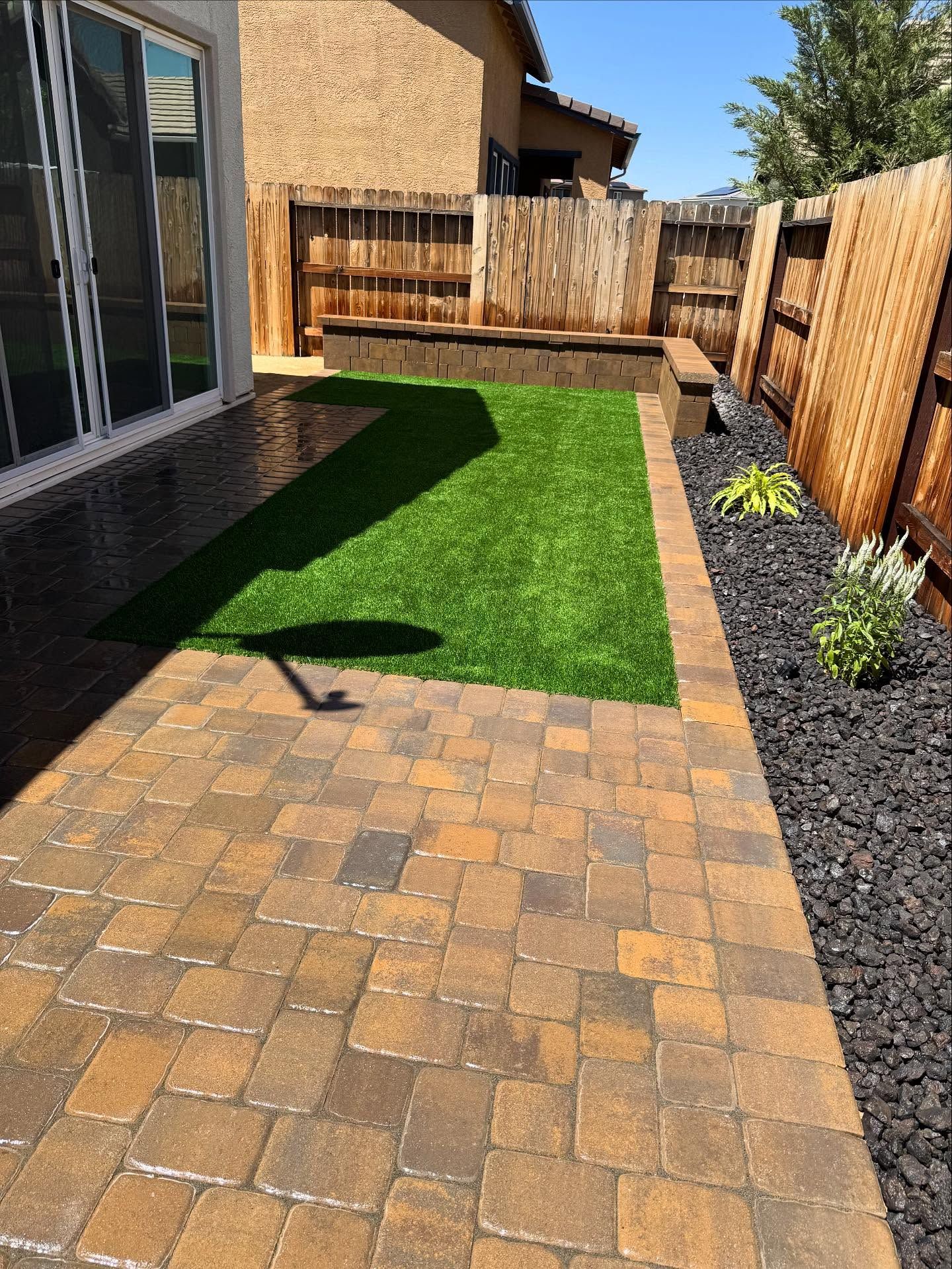 Patio with brick pavers, artificial turf, and a wooden fence.