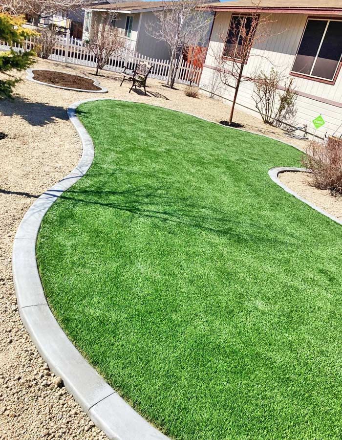 Green artificial lawn bordered by concrete, in a residential yard.