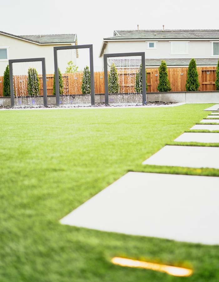 Modern backyard with rectangular water features, turf, and stone path.