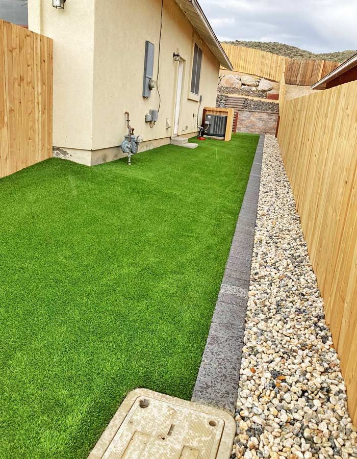 Backyard with artificial turf, gravel border, wooden fences, and house exterior.