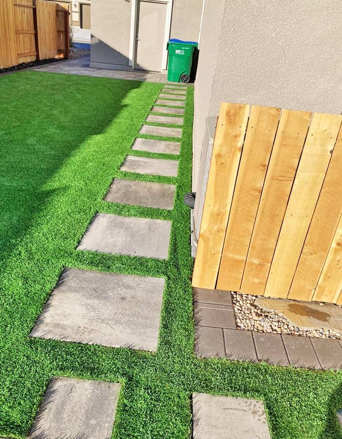 Square stepping stones on green turf lead to a trash can near a beige building.