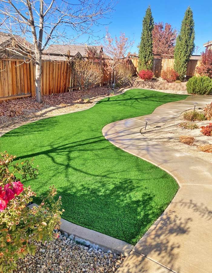 Green artificial turf yard with a winding concrete path and a wooden fence. Sunny day.