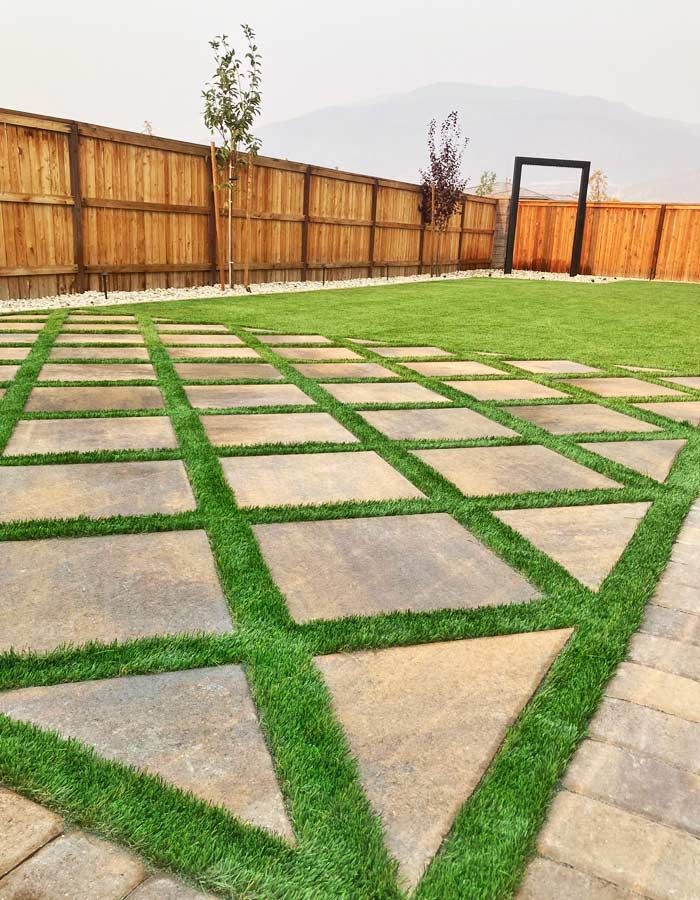 Lawn with square paving stones and green grass. Wooden fence and gate in background.