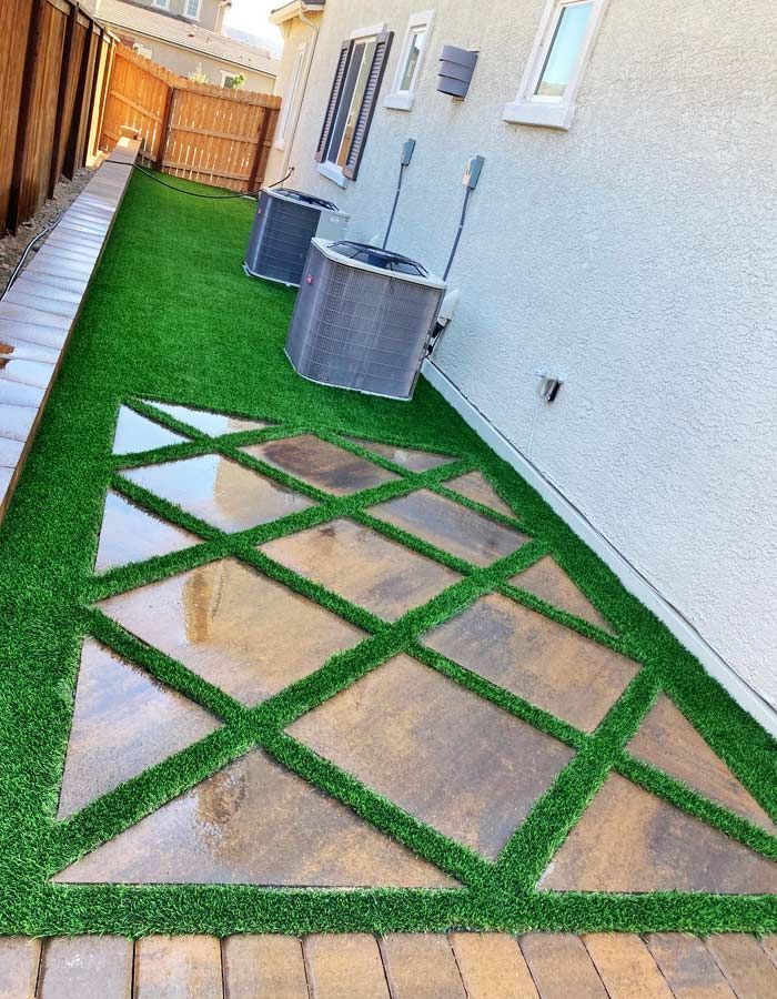 Artificial turf and stone pathway in a backyard, alongside a house wall and fence.