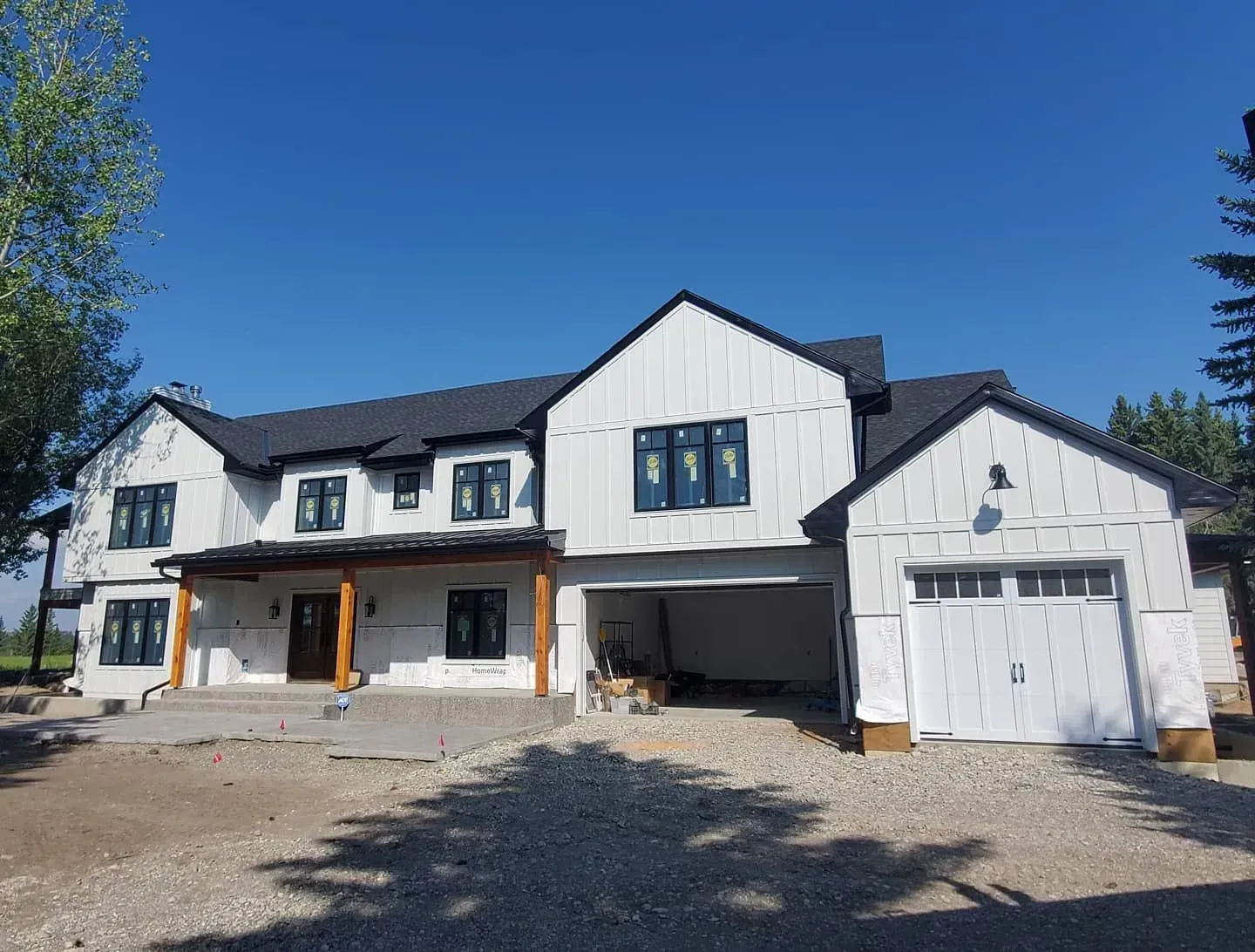 New white two-story house with black roof and garage under construction on a sunny day