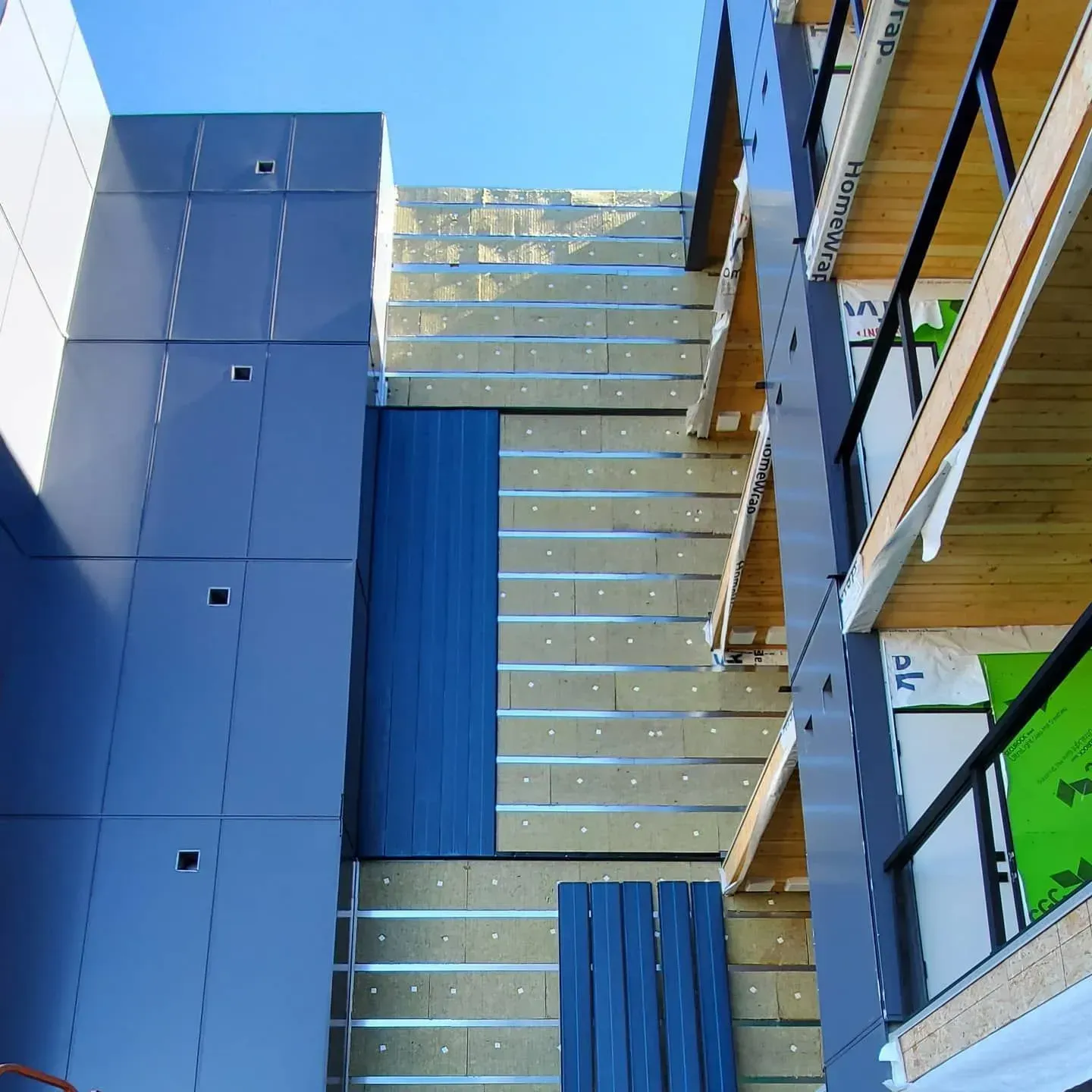 Modern building courtyard with blue panels, wood slats, and a glass walkway against a bright sky