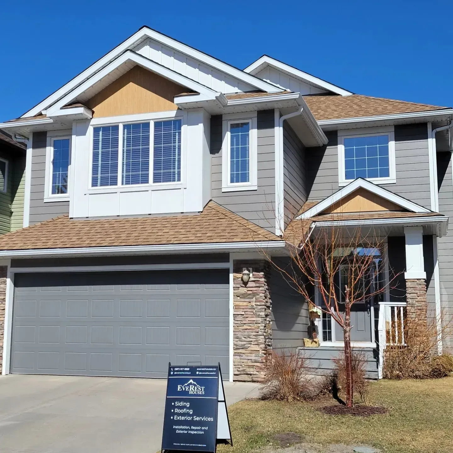 Two-story suburban house with gray garage, white trim, and a real estate sign in front