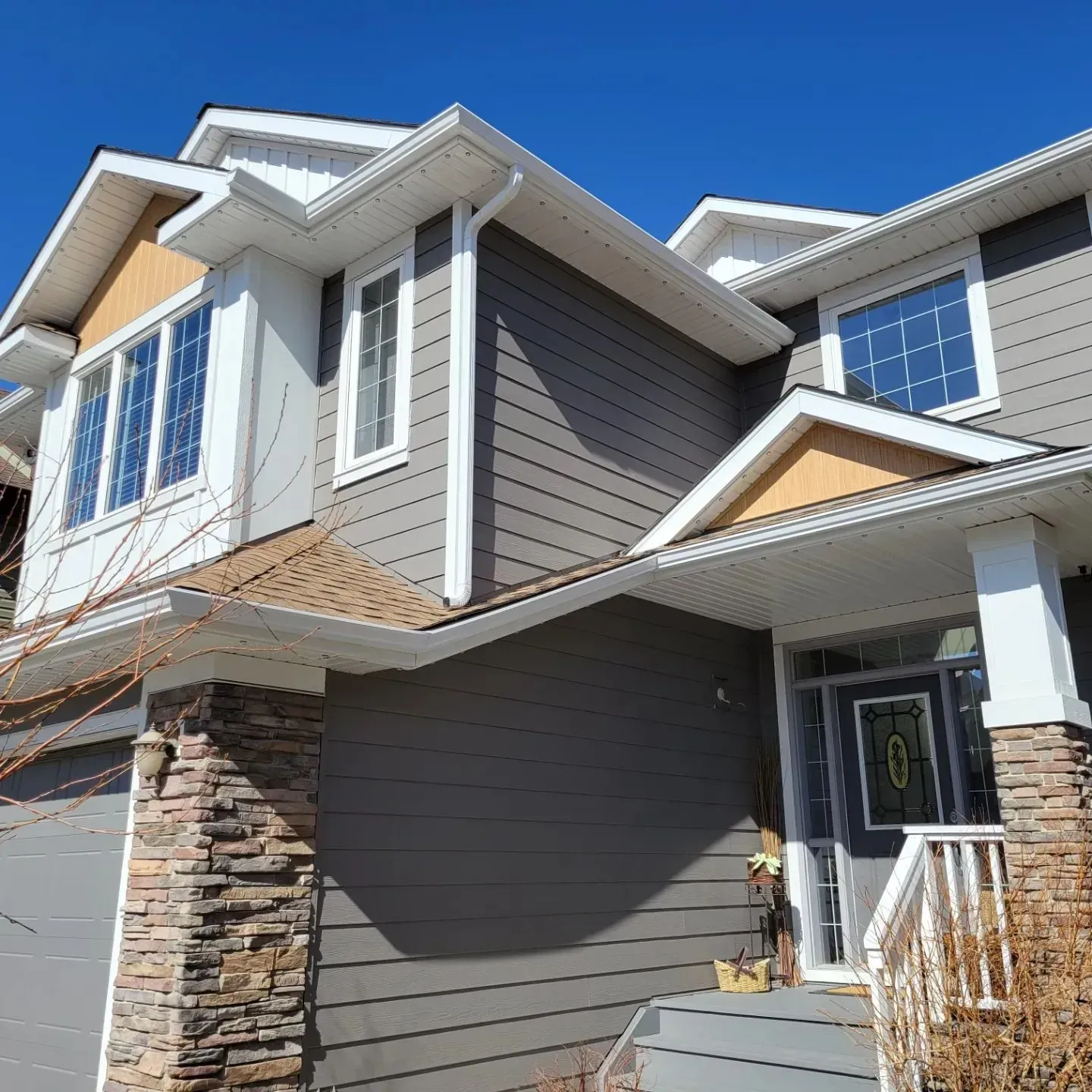 Two-story house exterior with gray siding, stone accents, white trim, and a blue sky backdrop