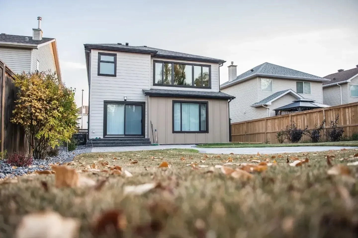 Modern two-story house with white siding and gray trim, viewed from a low angle across a backyard.