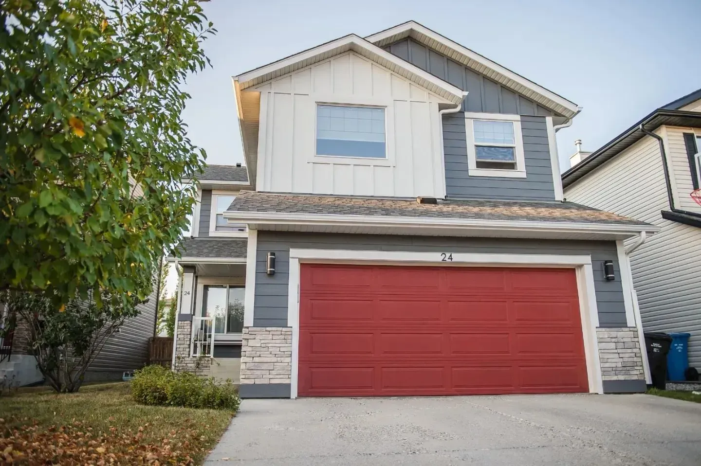 Two-story house with red garage door and gray siding, viewed from the street