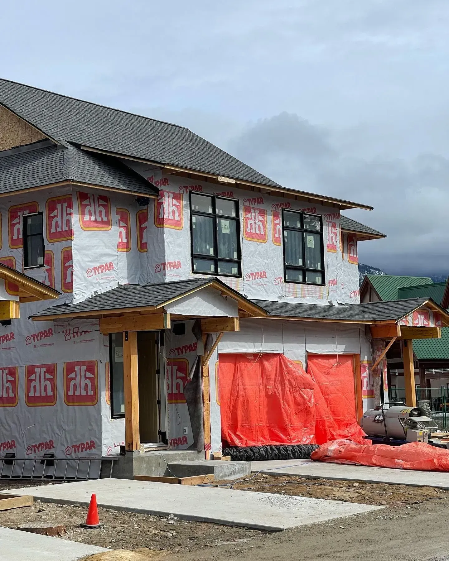 House under construction wrapped in protective plastic, with scaffolding and a gray roof in a rural setting