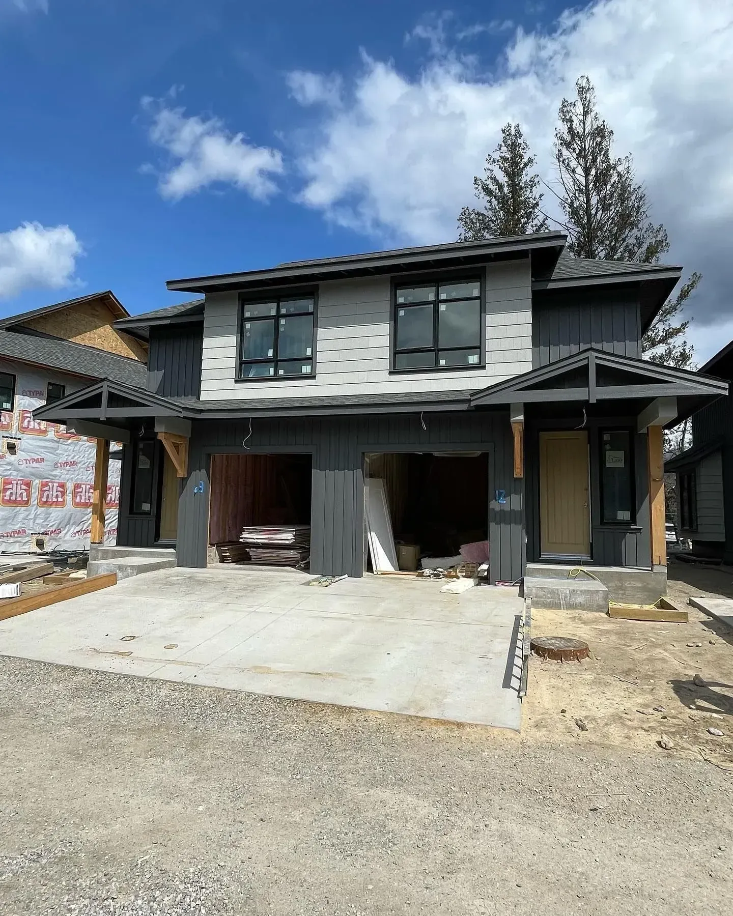 New two-story gray house under construction with open garage and driveway under a blue sky