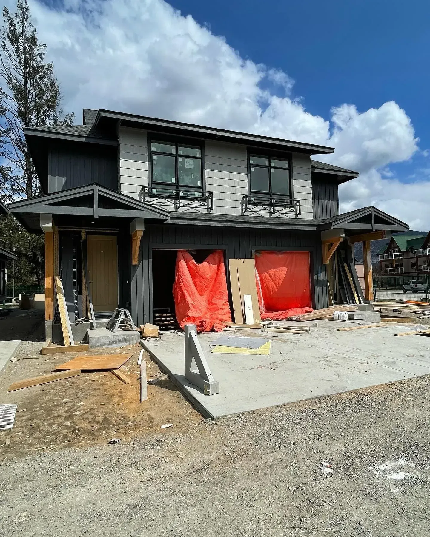 Two-story house under construction with red garage coverings and unfinished front driveway