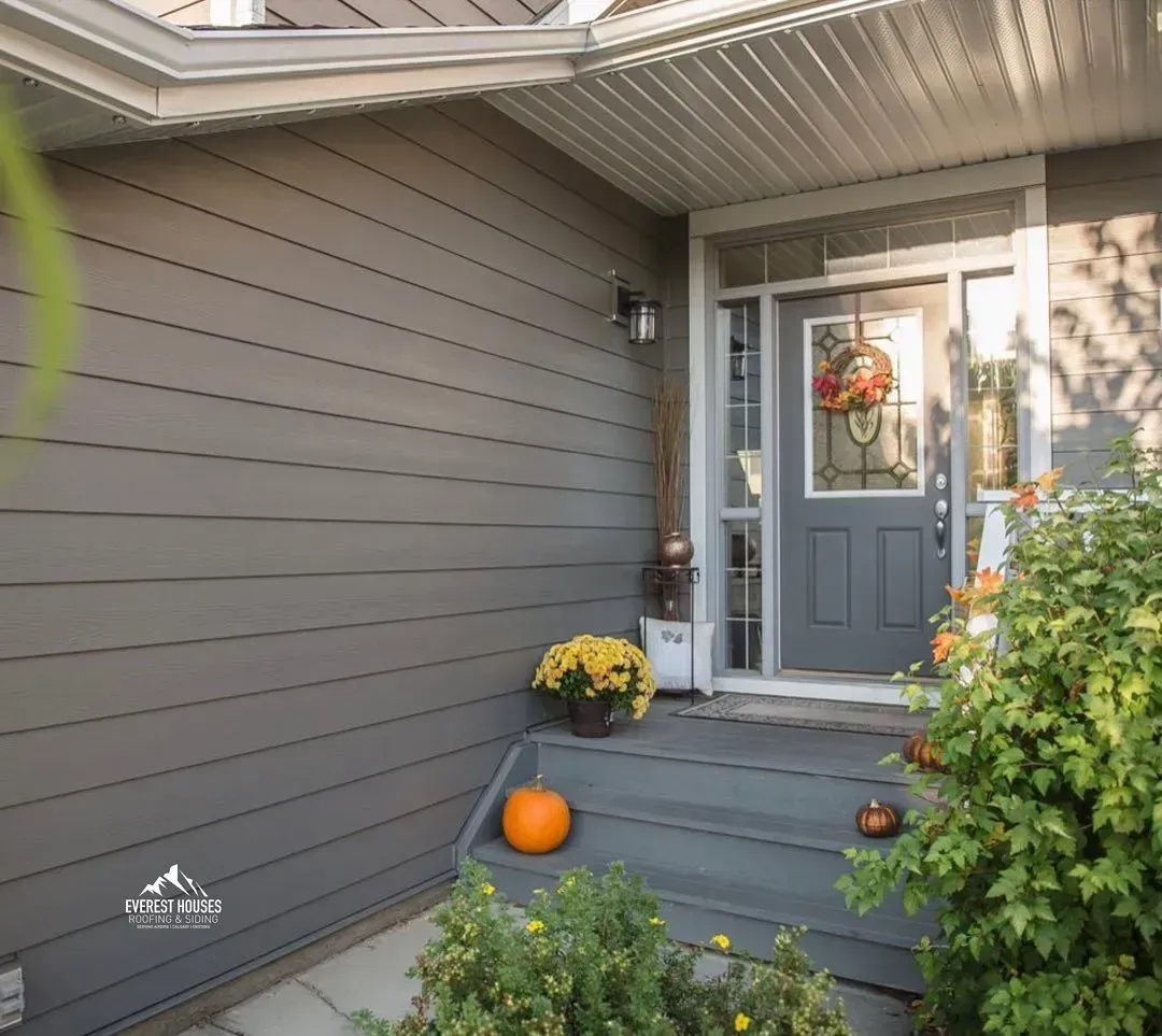Front porch with gray siding, blue door, pumpkins, and yellow flowers at the entryway