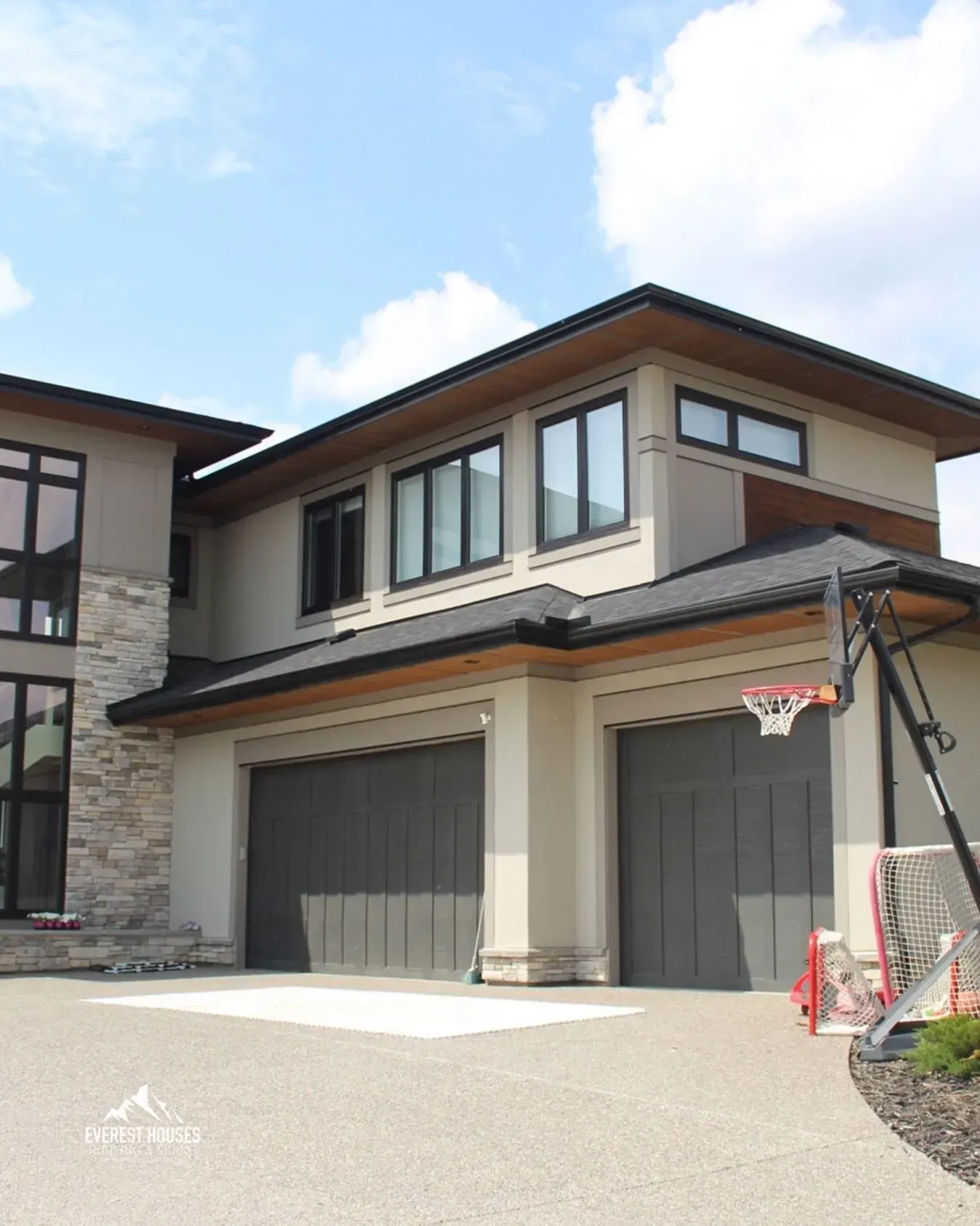 Modern two-story house exterior with garage doors and a basketball hoop on the driveway