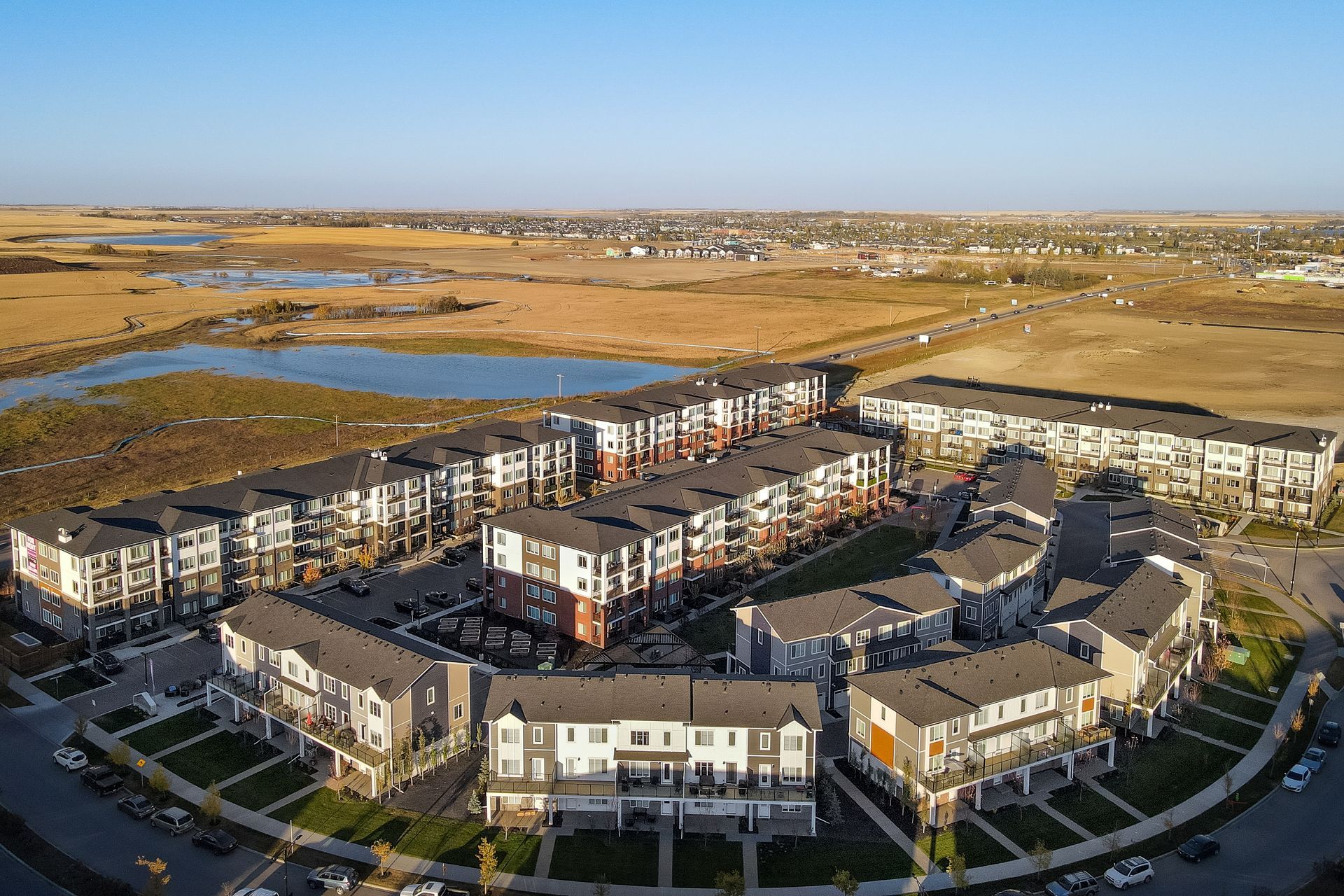 Aerial view of a modern apartment complex beside wetlands and open fields at sunset
