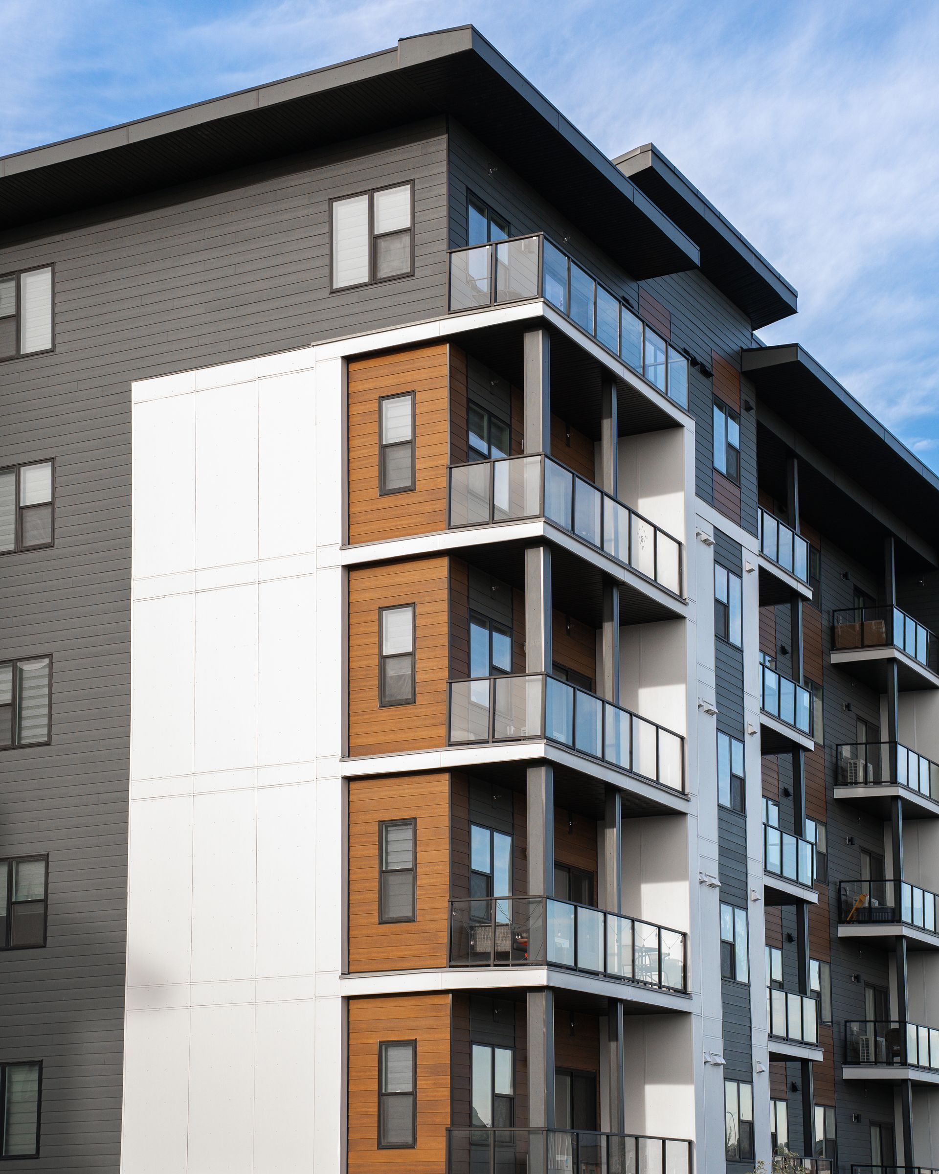 Modern apartment building with balconies and dark gray and white exterior against a blue sky