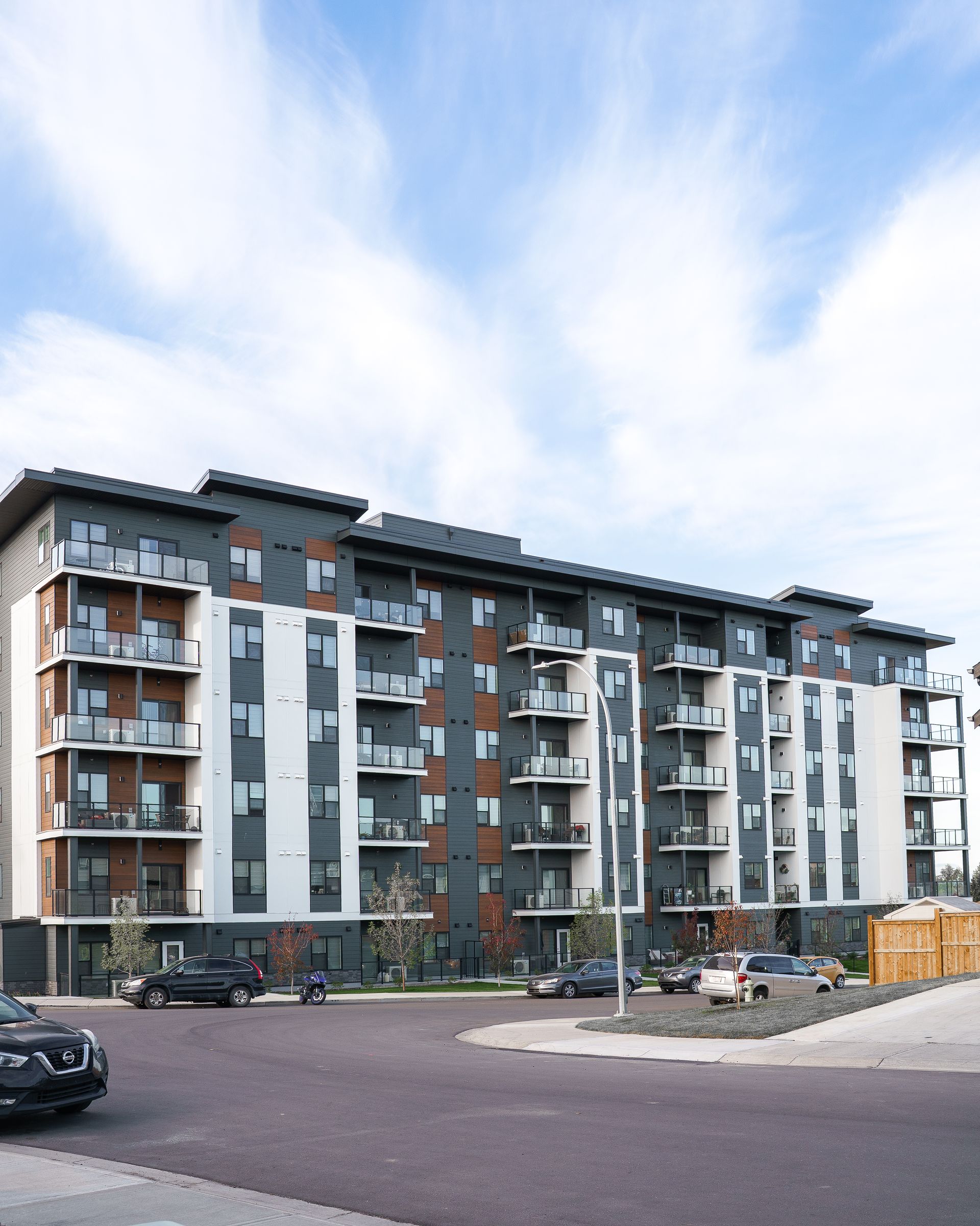 Modern apartment building with balconies and parked cars under a cloudy sky