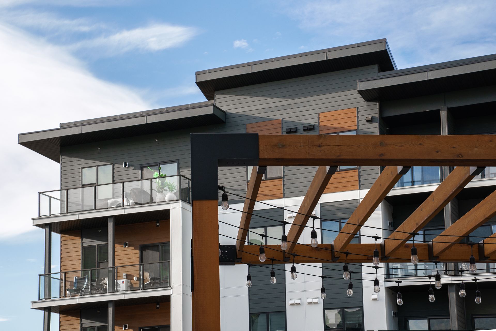 Modern apartment building with balconies and a wooden pergola under a cloudy sky