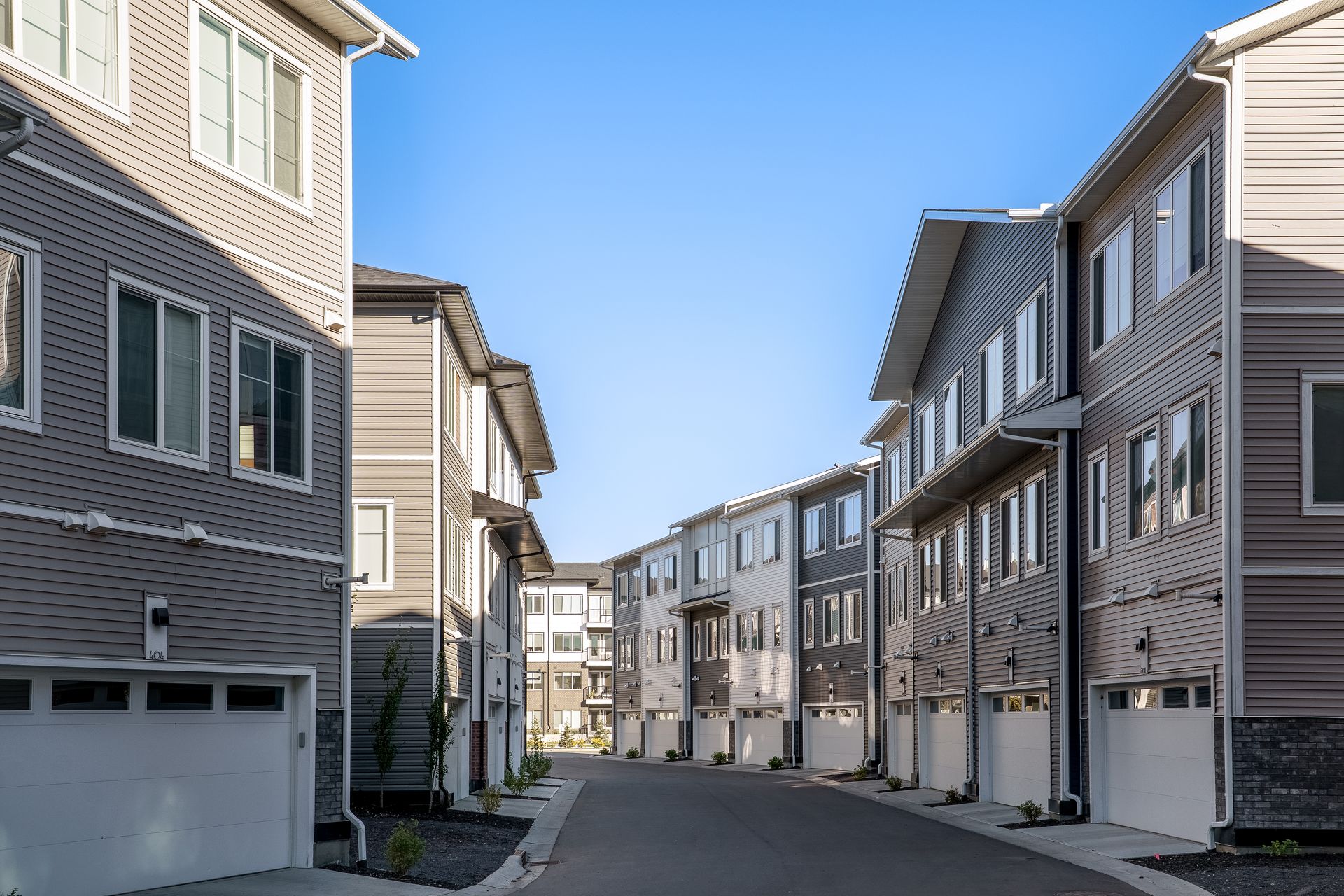Row of modern beige townhouses along a quiet residential street under a clear blue sky