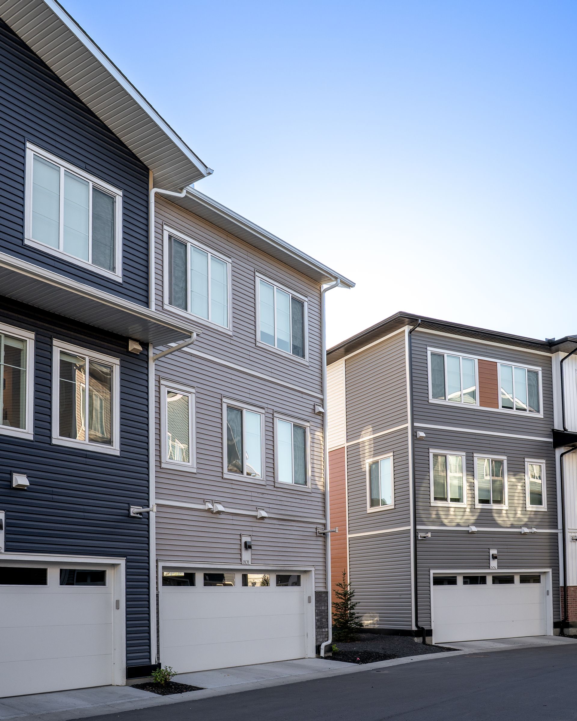Row of gray modern townhouses with white garages under a clear blue sky