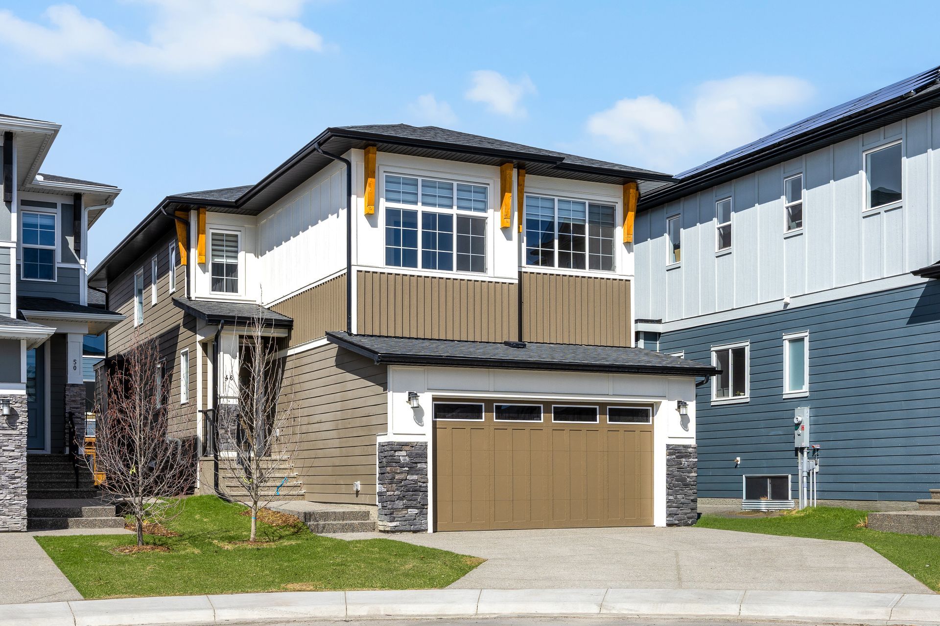 Modern two-story suburban house with tan garage doors, wood-accent balcony, and blue siding