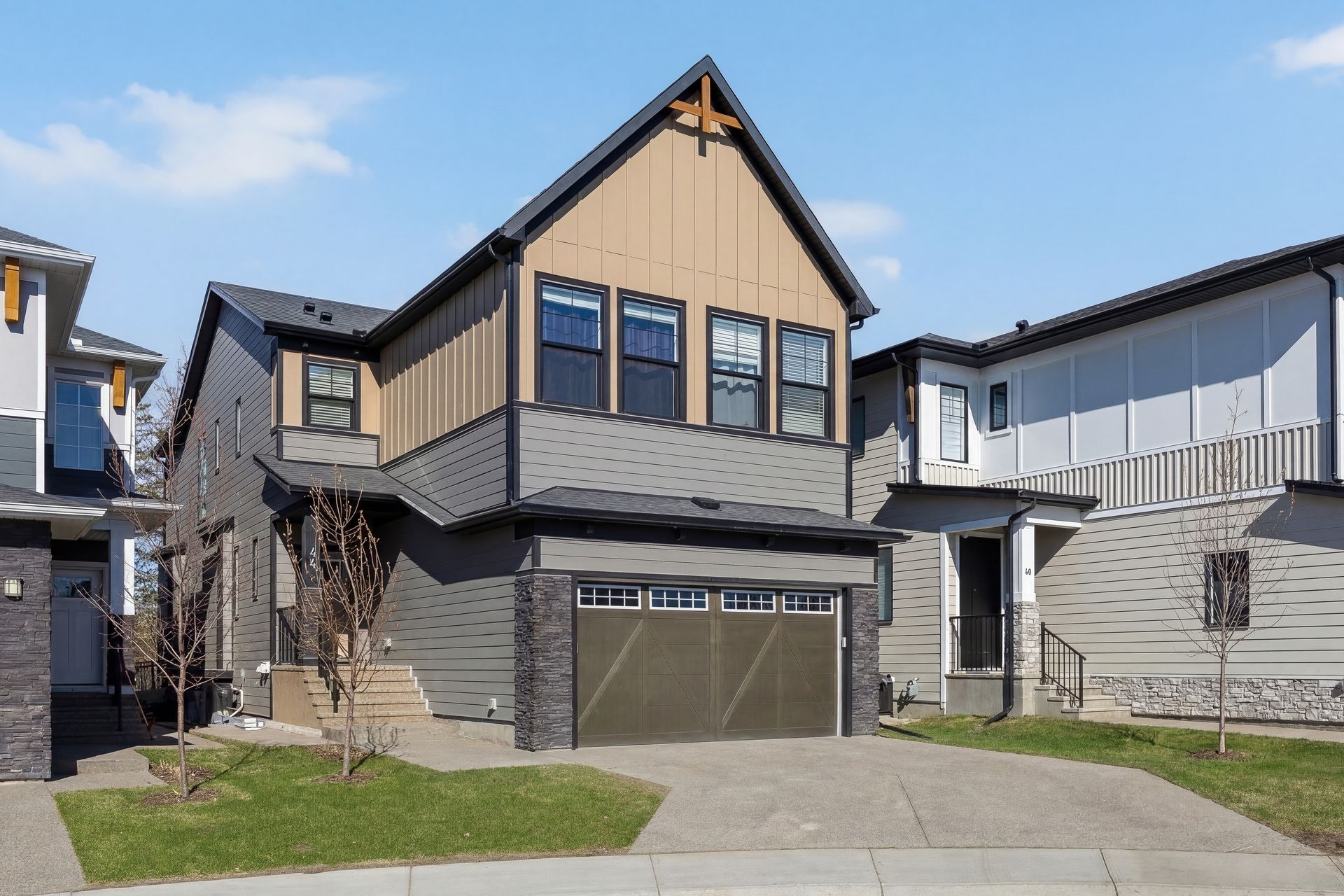 Modern two-story house with beige siding, stone accents, and a double garage on a suburban street