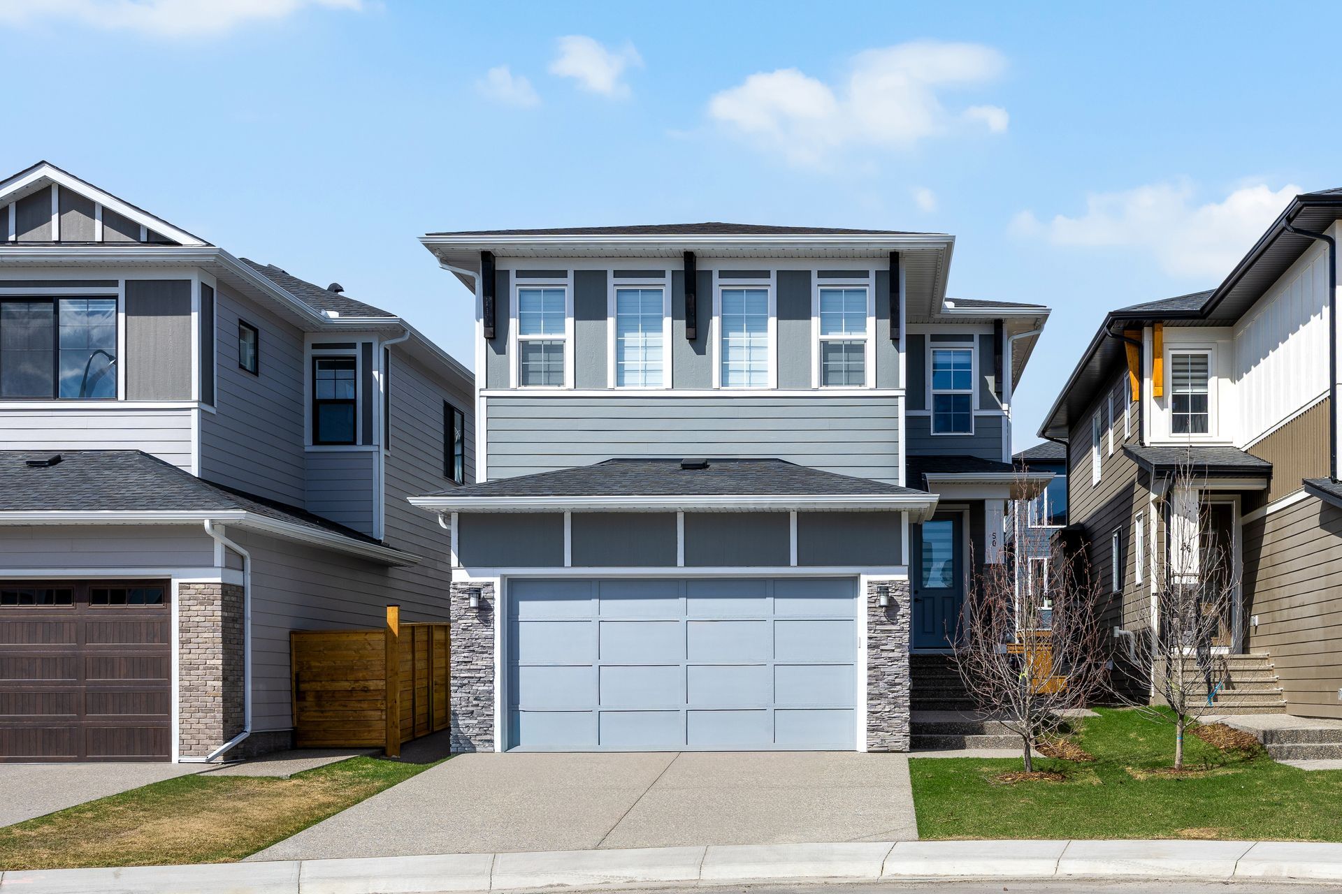Two-story suburban house with a gray exterior, attached garage, and driveway under a blue sky.