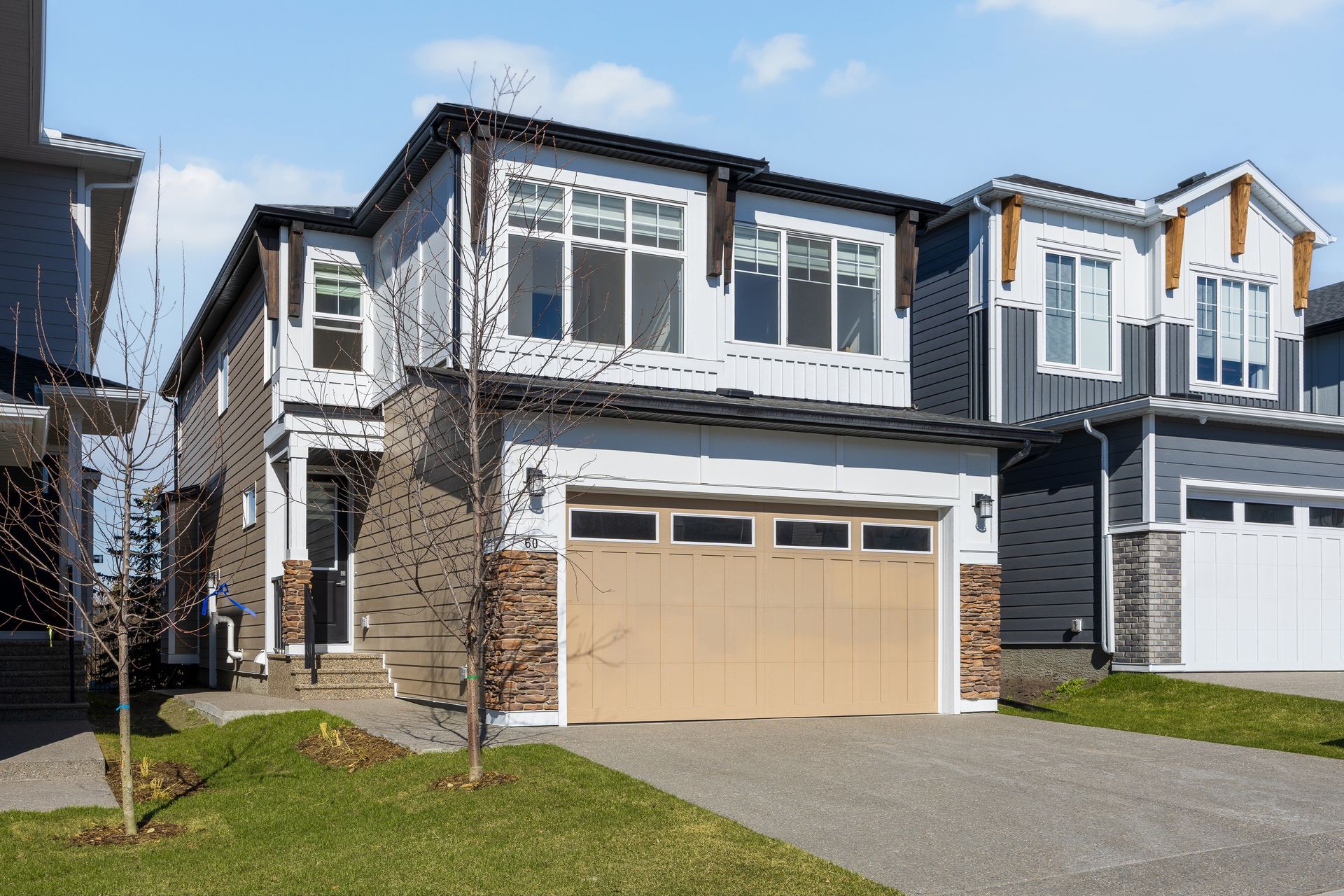 Modern two-story suburban house with beige garage, white trim, and a green lawn under a blue sky